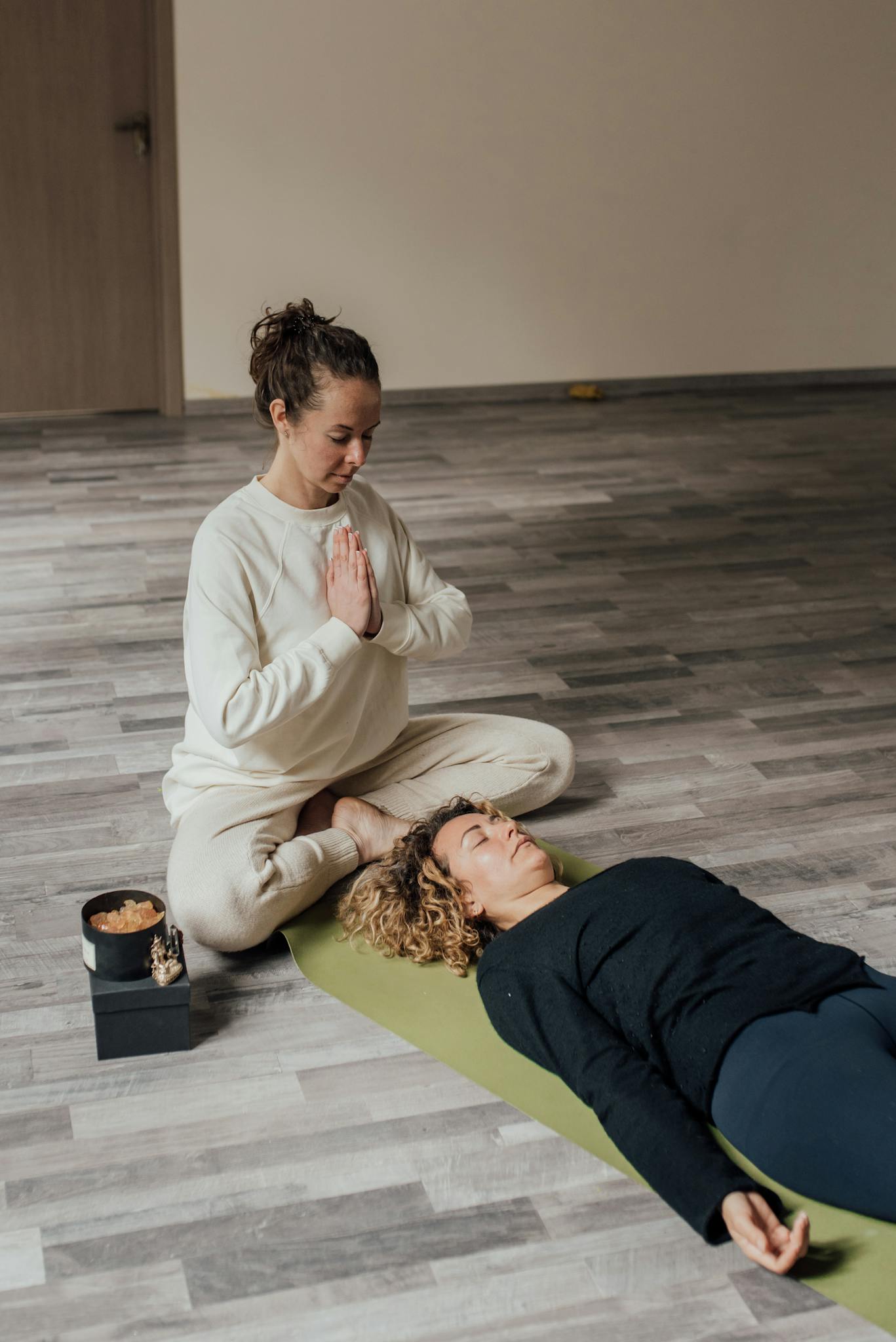 A peaceful indoor meditation session with a guide and a participant on a yoga mat.