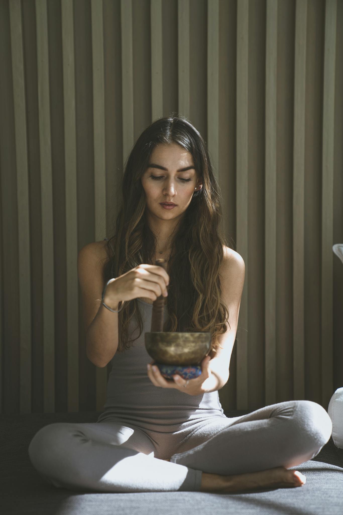 Woman in meditation holding a singing bowl in a serene indoor setting, capturing tranquility and mindfulness.